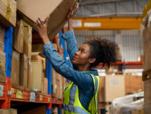 female warehouse worker grabbing for box above her head